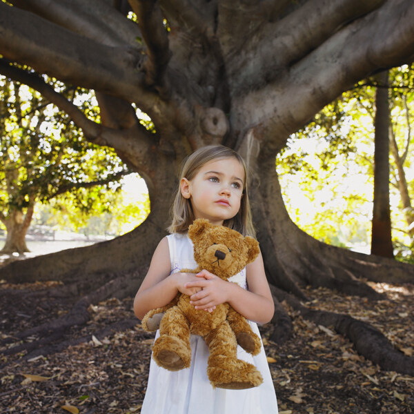 大树下抱着布娃娃的可爱小女孩图片