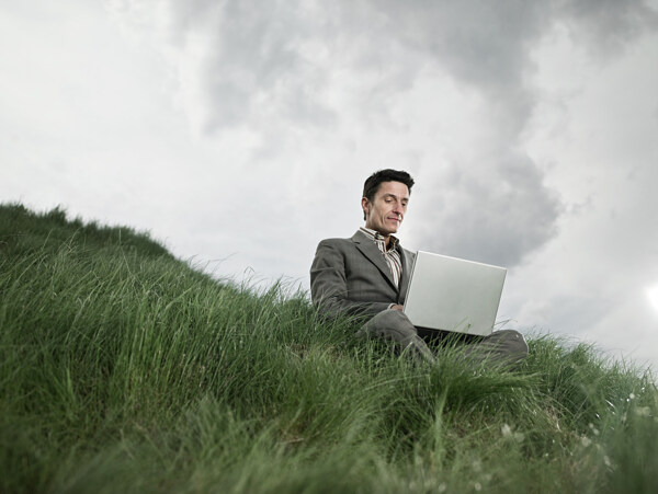 草地上玩电脑的男人图片